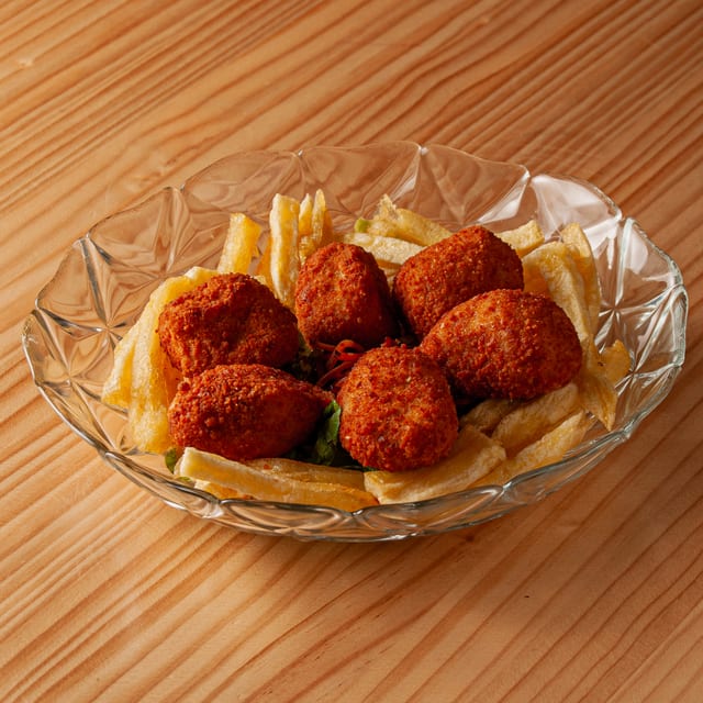 Plato de cristal con varias croquetas de jamón doradas y crujientes acompañadas de patatas fritas sobre una mesa de madera.