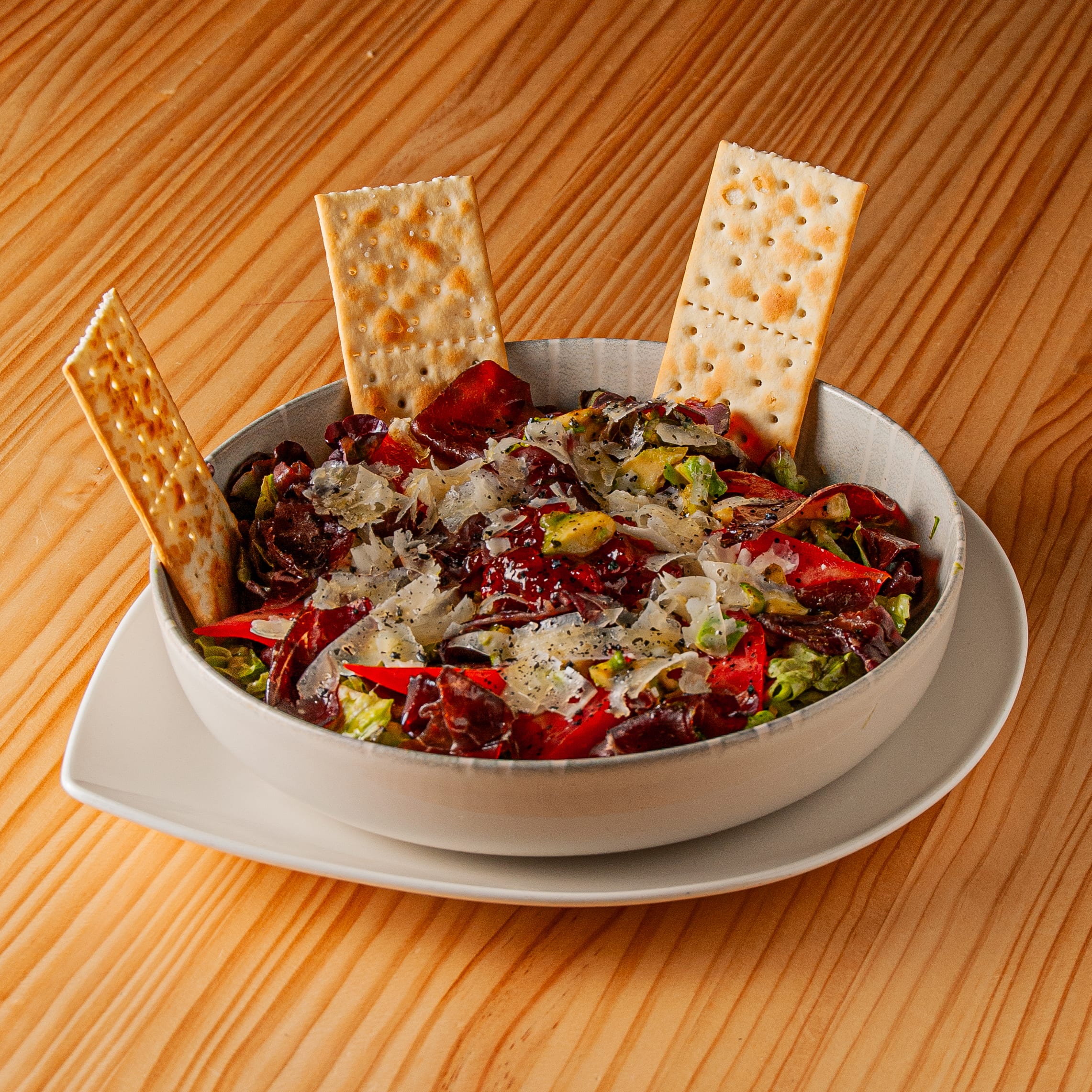 Ensalada de cecina servida en cuenco cerámico con lascas de queso curado y acompañamiento de galletas saladas sobre mesa de madera.