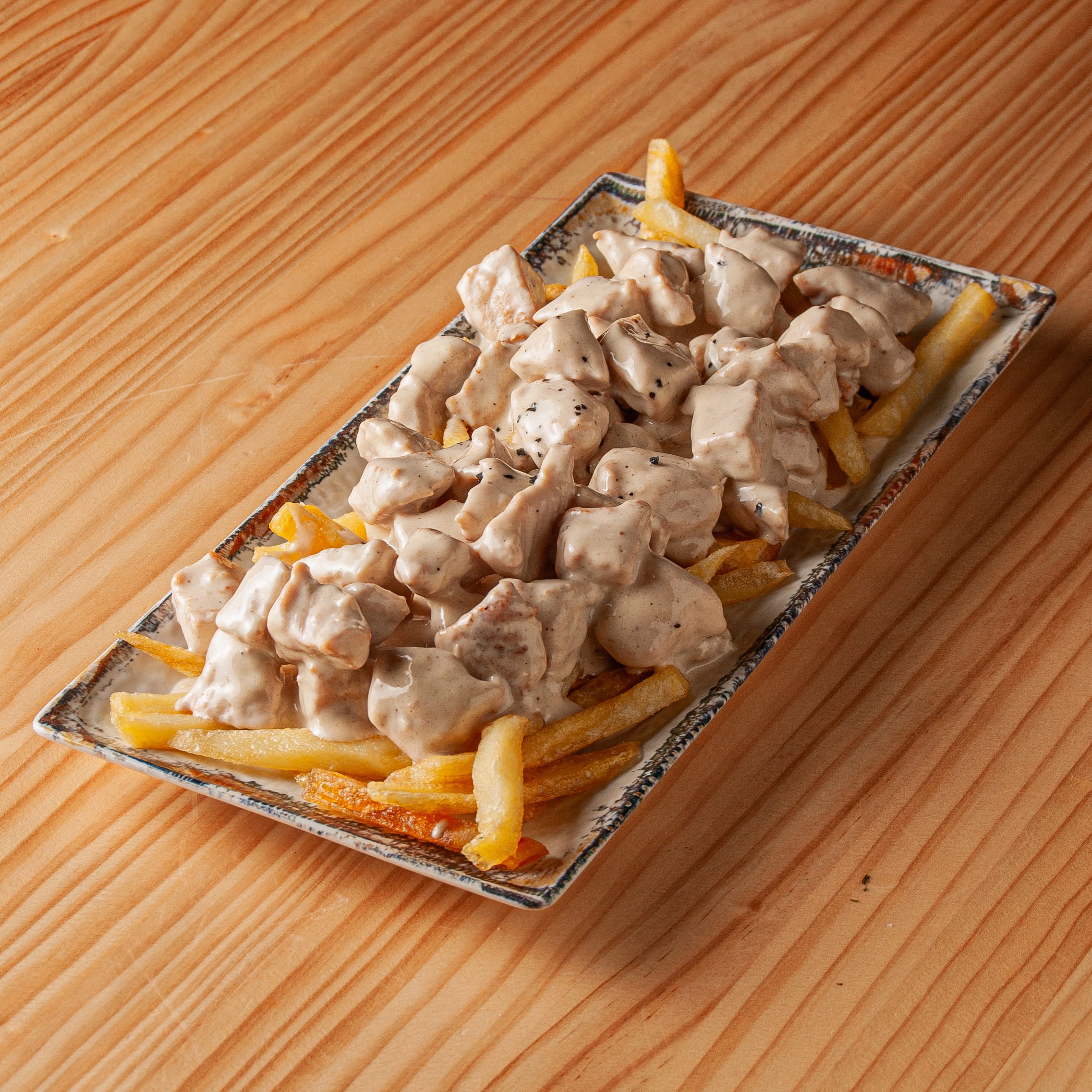 Ración de raxo con salsa de queso Cabrales servida sobre una base de patatas fritas en una bandeja rectangular sobre mesa de madera.