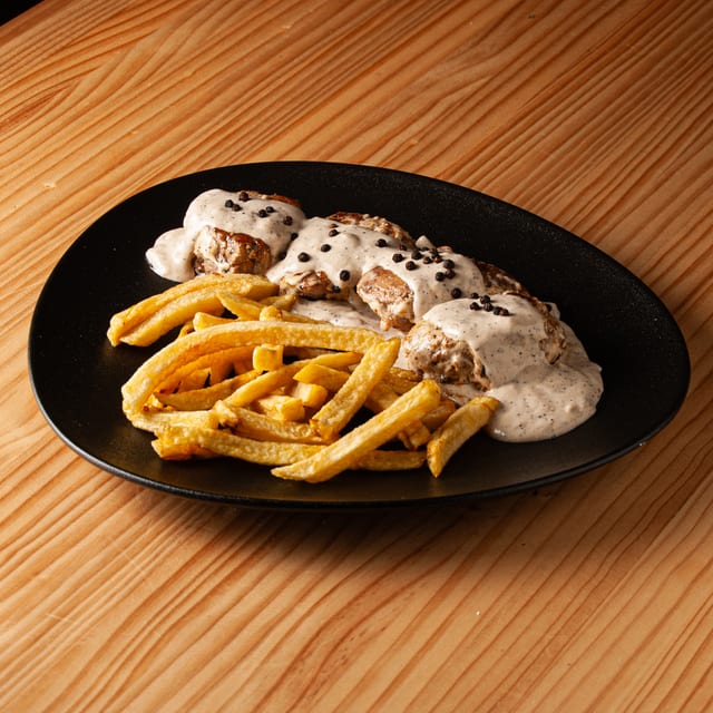 Ración de solomillo a la pimienta con guarnición de patatas fritas sobre plato negro.