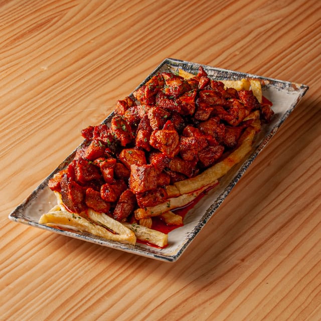 Ración de zorza adobada con pimentón servida sobre una cama de patatas fritas en una bandeja rectangular sobre mesa de madera.